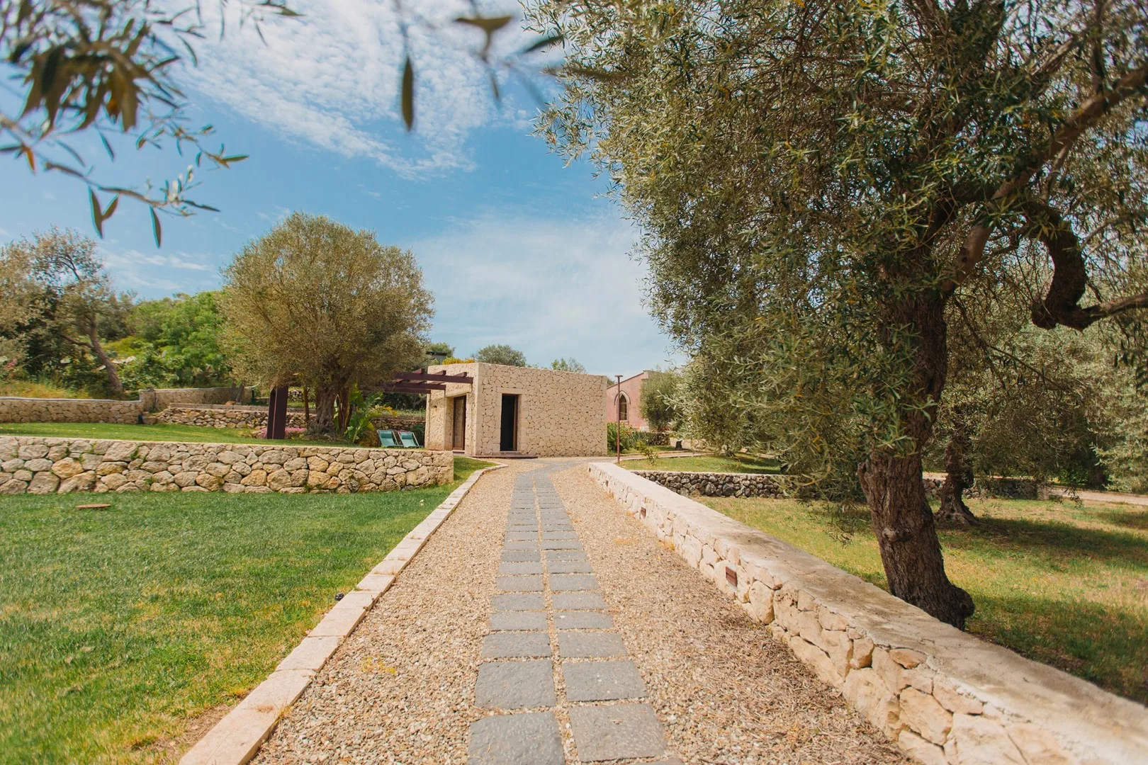 Un camino de piedra conduce a un edificio pequeño entre zonas verdes.
