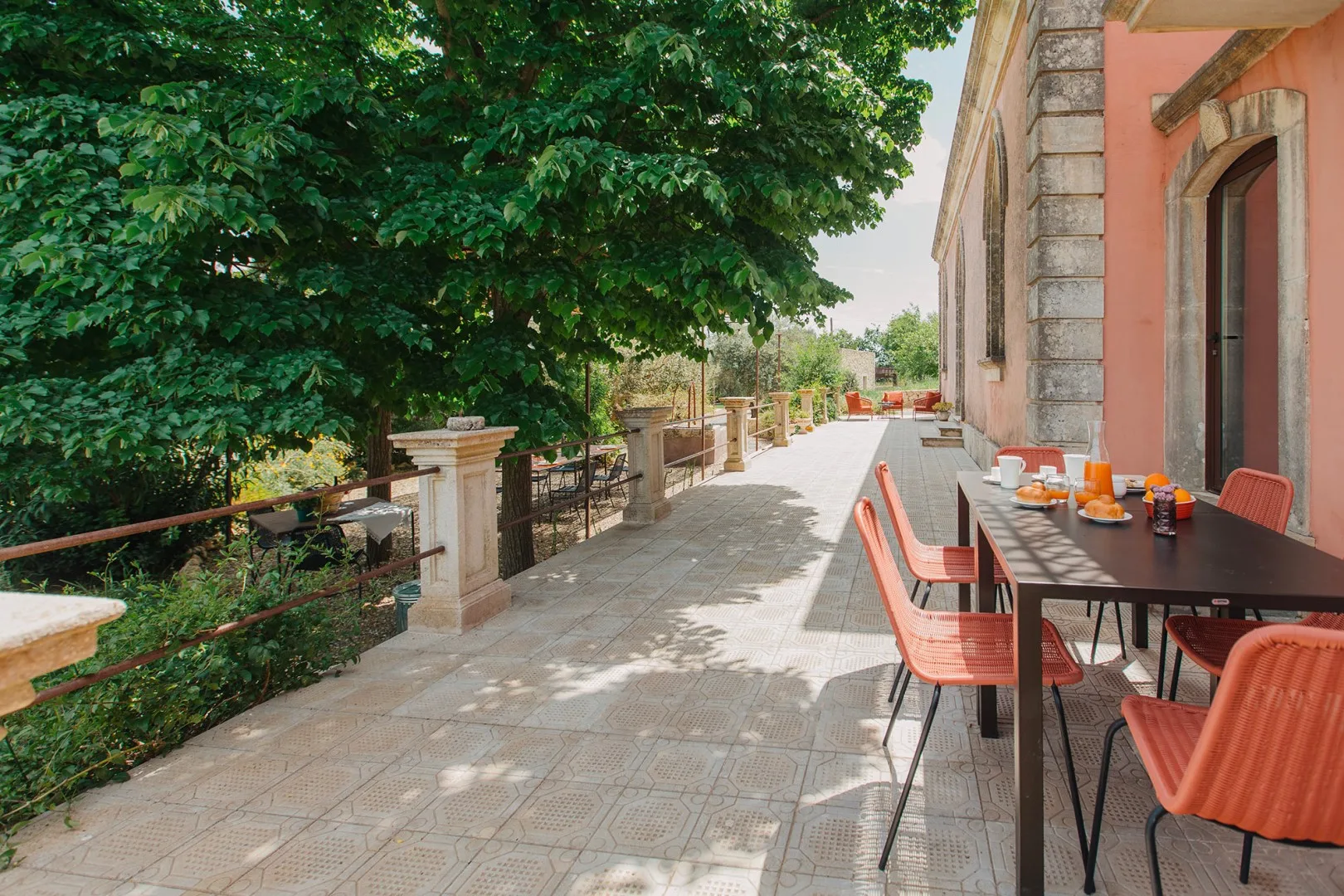 Una terraza pavimentada tiene mesas y asientos junto a un sendero arbolado.