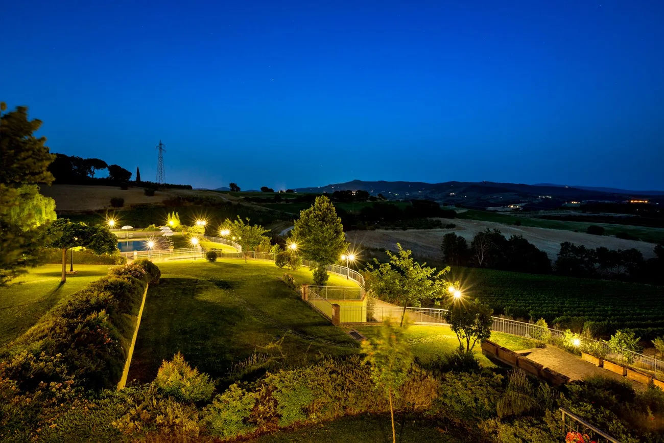 A landscaped garden with illuminated paths overlooks fields at dusk.
