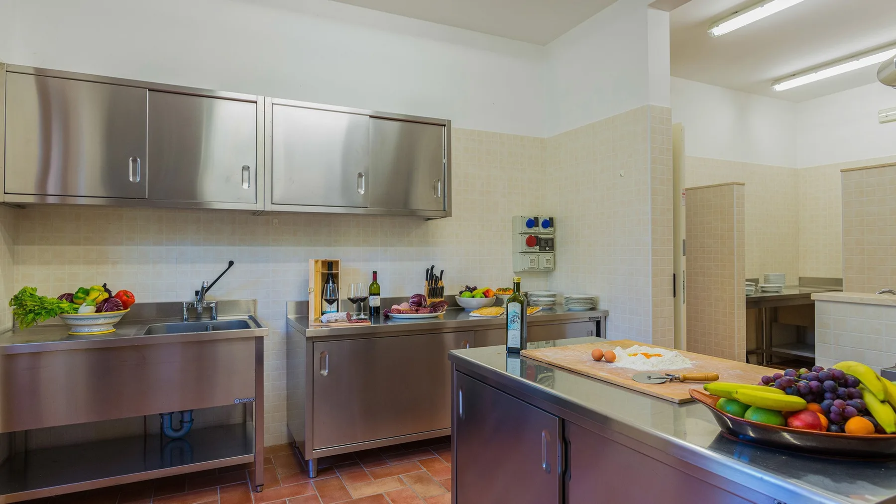 A commercial kitchen with stainless steel counters and fresh produce on the work surfaces.