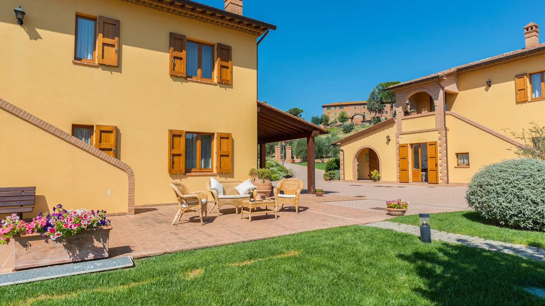 A sunny courtyard with outdoor seating, flower planters, and surrounding buildings.