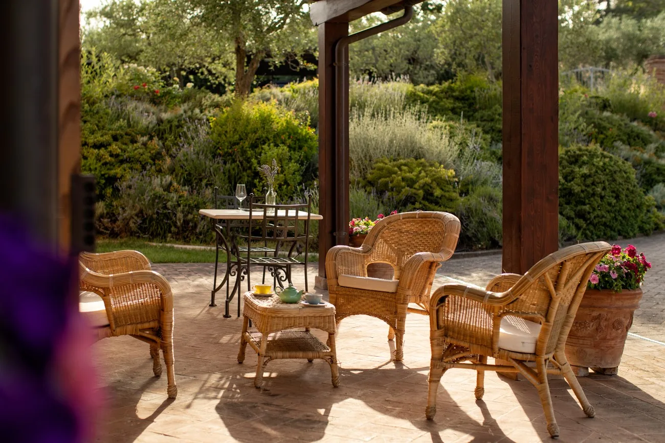 A covered patio with wicker seating and a small outdoor table overlooks a garden.
