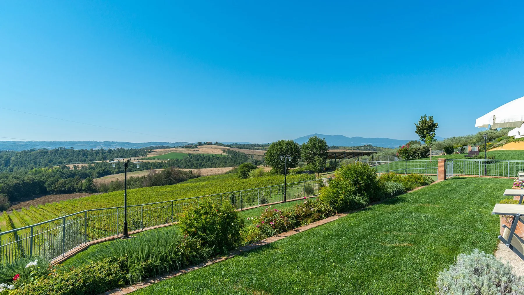 A landscaped garden overlooks green fields and distant hills under a clear sky.