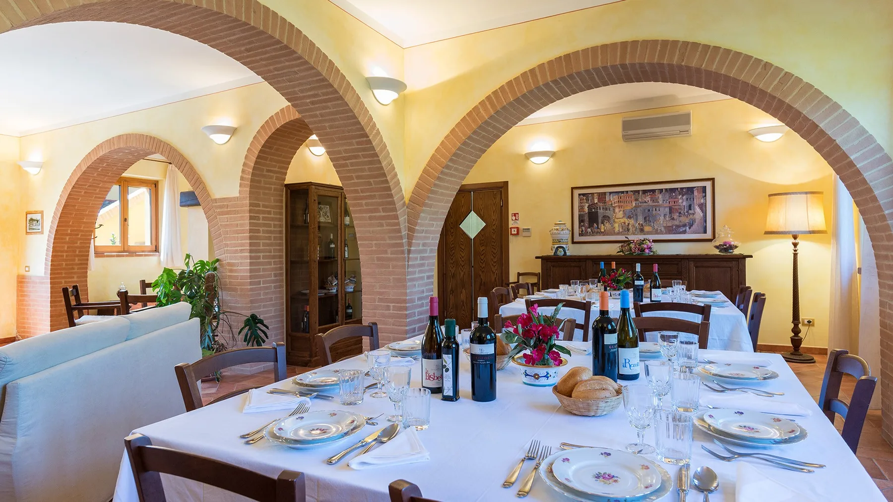 A dining room with a long table set with dishes beneath brick arches.