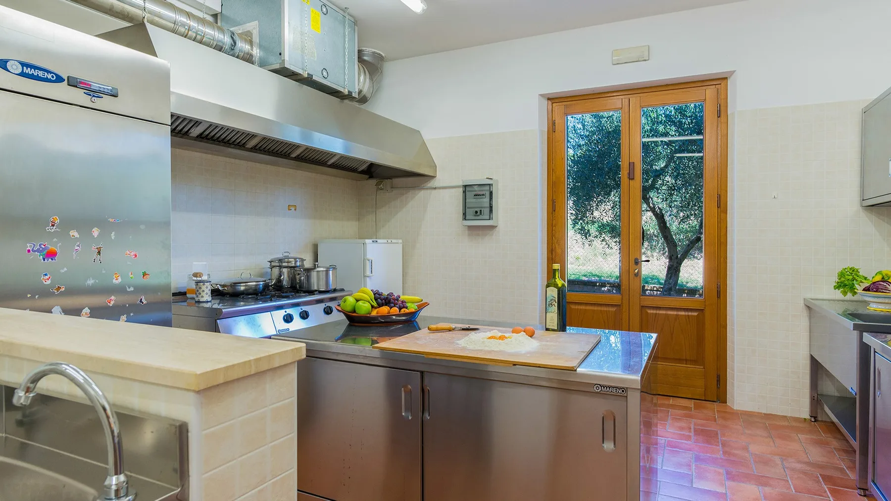 A kitchen with a central work counter, cooking equipment, and a glazed wooden door.