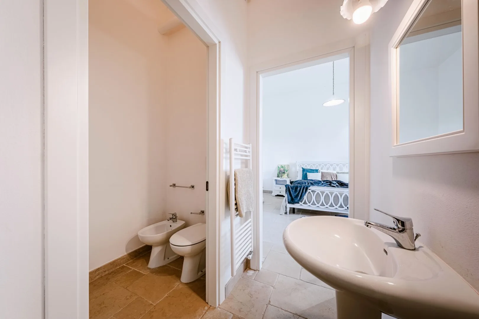La puerta del baño da a un dormitorio; se ven un lavabo, un inodoro, un bidé y un toallero radiador.