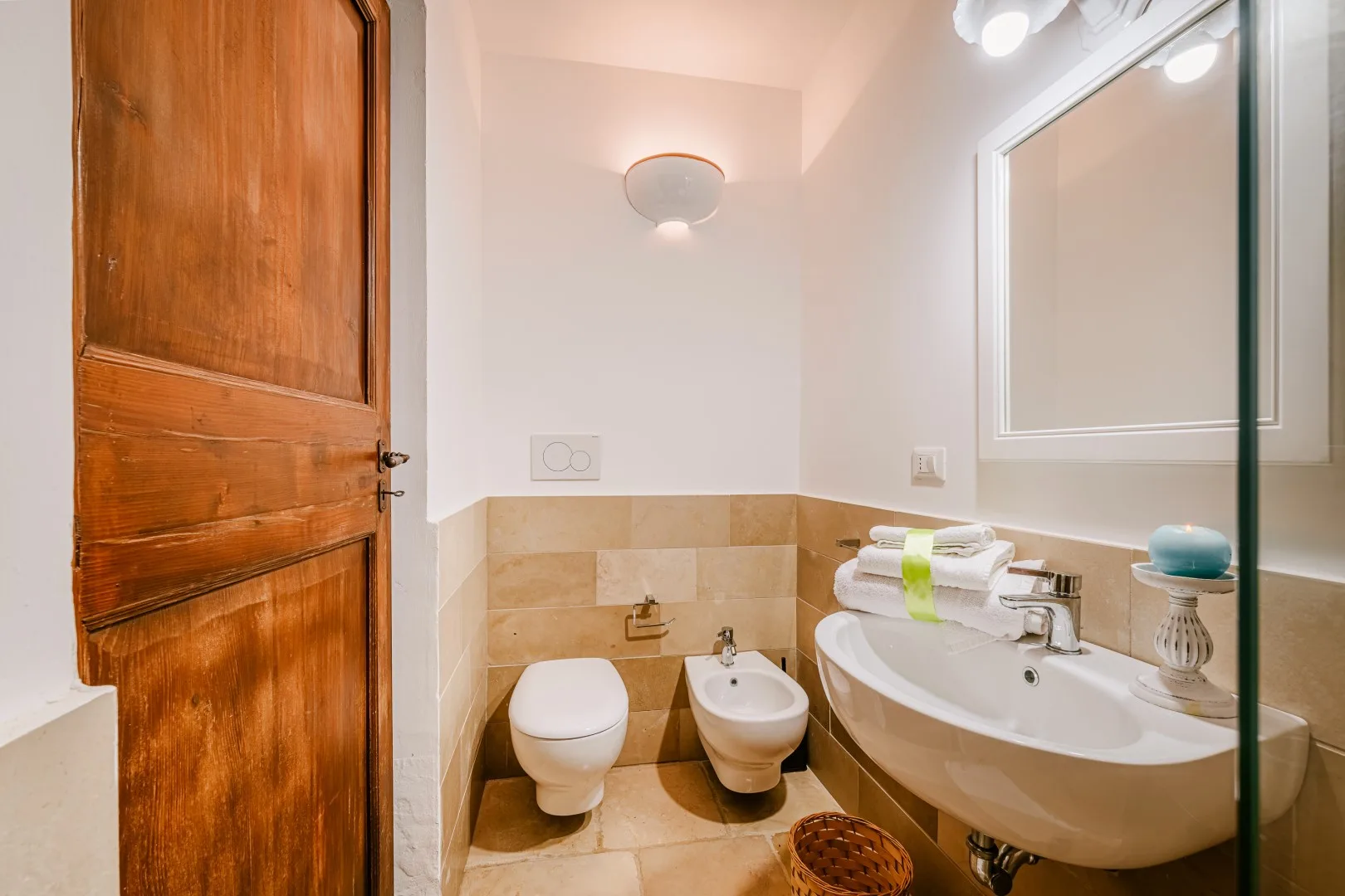 Un baño con puerta de madera, paredes de azulejos beige, bañera y bidé.
