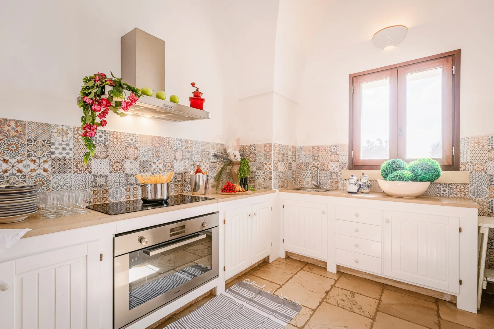 Una cocina luminosa con armarios blancos, azulejos estampados, un horno empotrado y una ventana sobre la encimera.