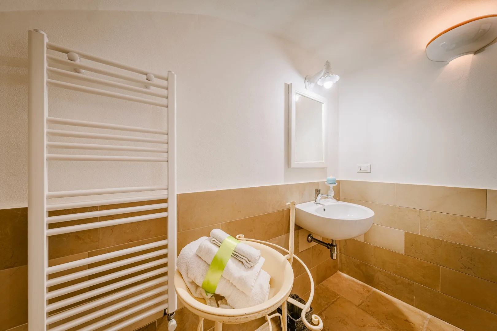 Un baño alicatado cuenta con un lavabo de pared, un toallero calefactable y toallas dobladas en una cesta.