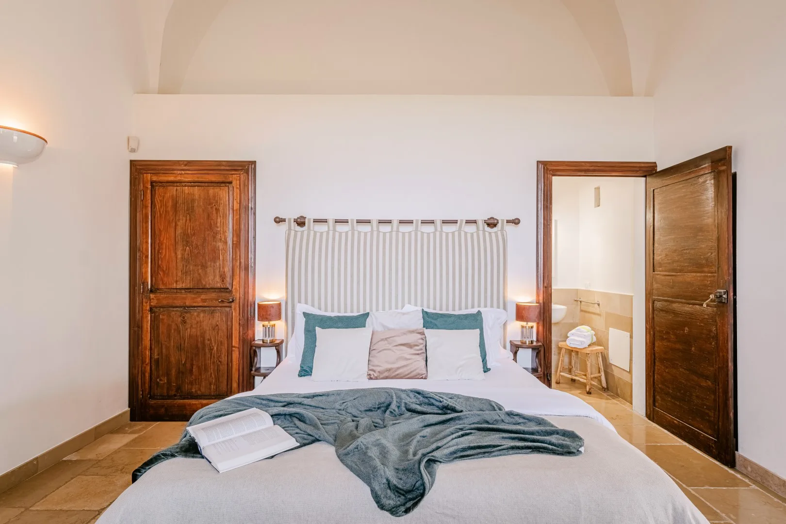 Un dormitorio con una cama doble, ropa de cama verde azulado, puertas de madera y un radiador blanco alto detrás del cabecero.