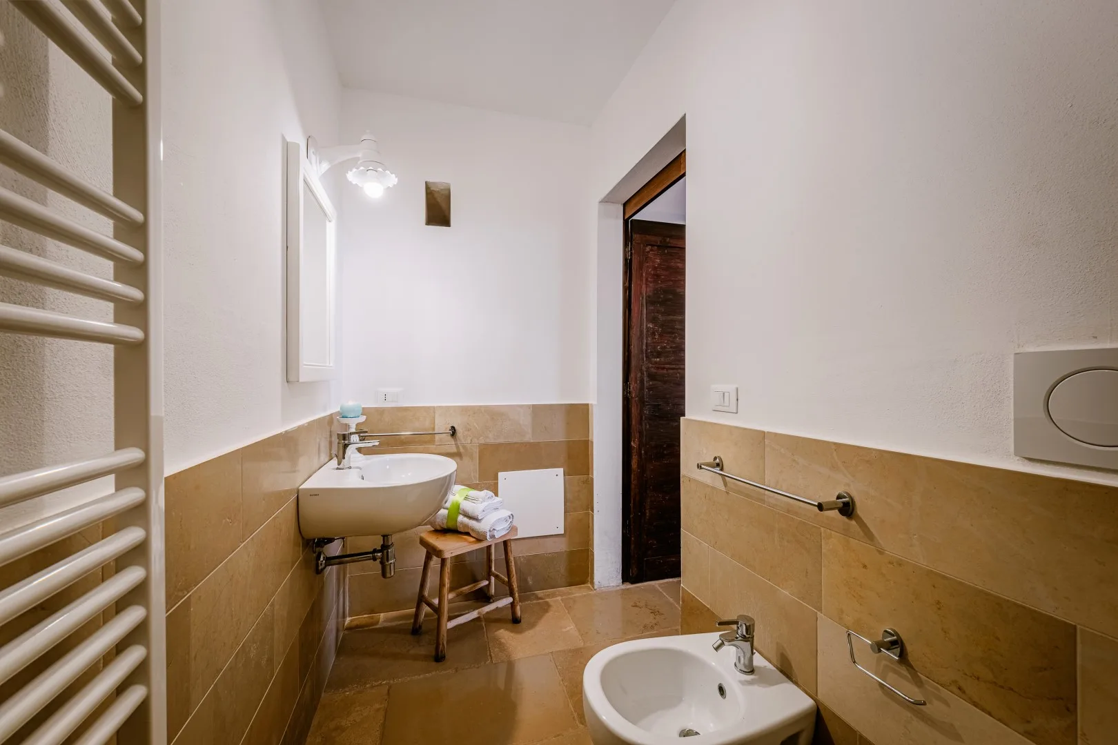 Un baño con azulejos, lavabo de pared, bidé y toallero calefactor junto a la puerta.