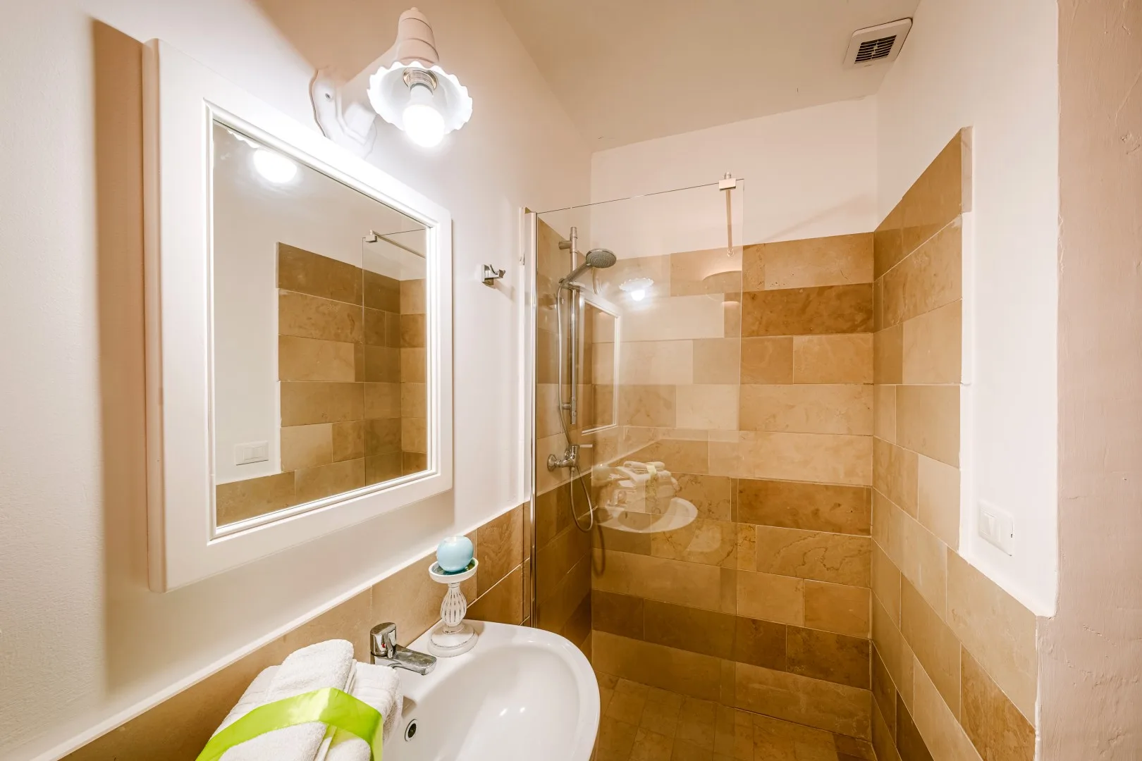 Baño alicatado con lavabo blanco, espejo iluminado y mampara de ducha de vidrio.