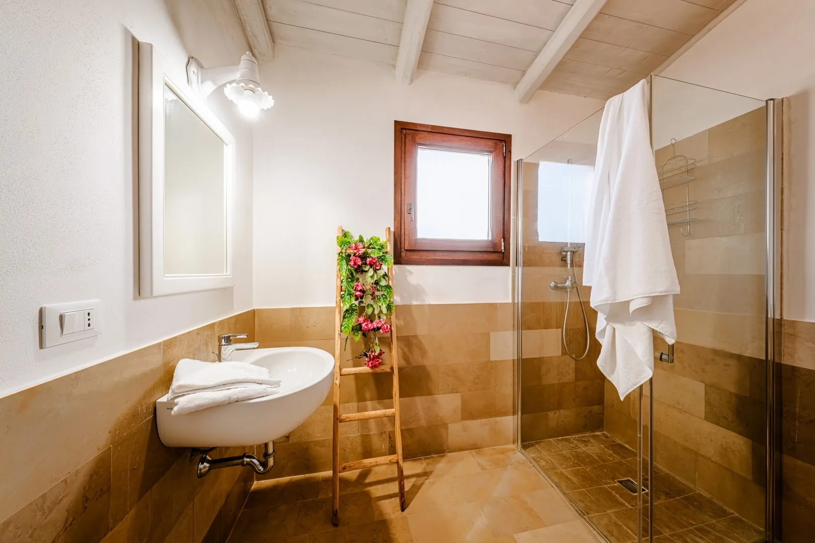 Un baño alicatado cuenta con un lavabo suspendido, una ducha de vidrio y una ventana pequeña.