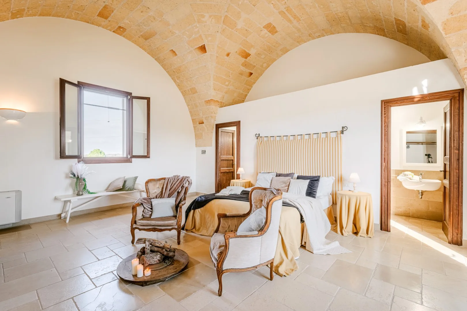 Dormitorio con techo abovedado de piedra, una cama grande y dos sillones tapizados.