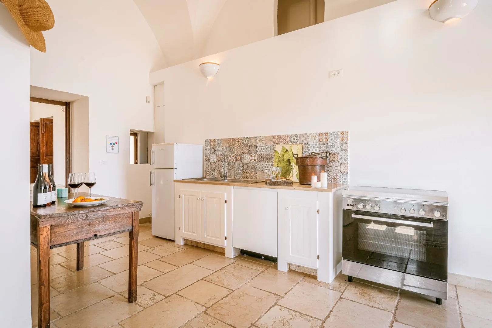 Una cocina luminosa con armarios blancos, un salpicadero de azulejos, una estufa y una pequeña mesa de madera.