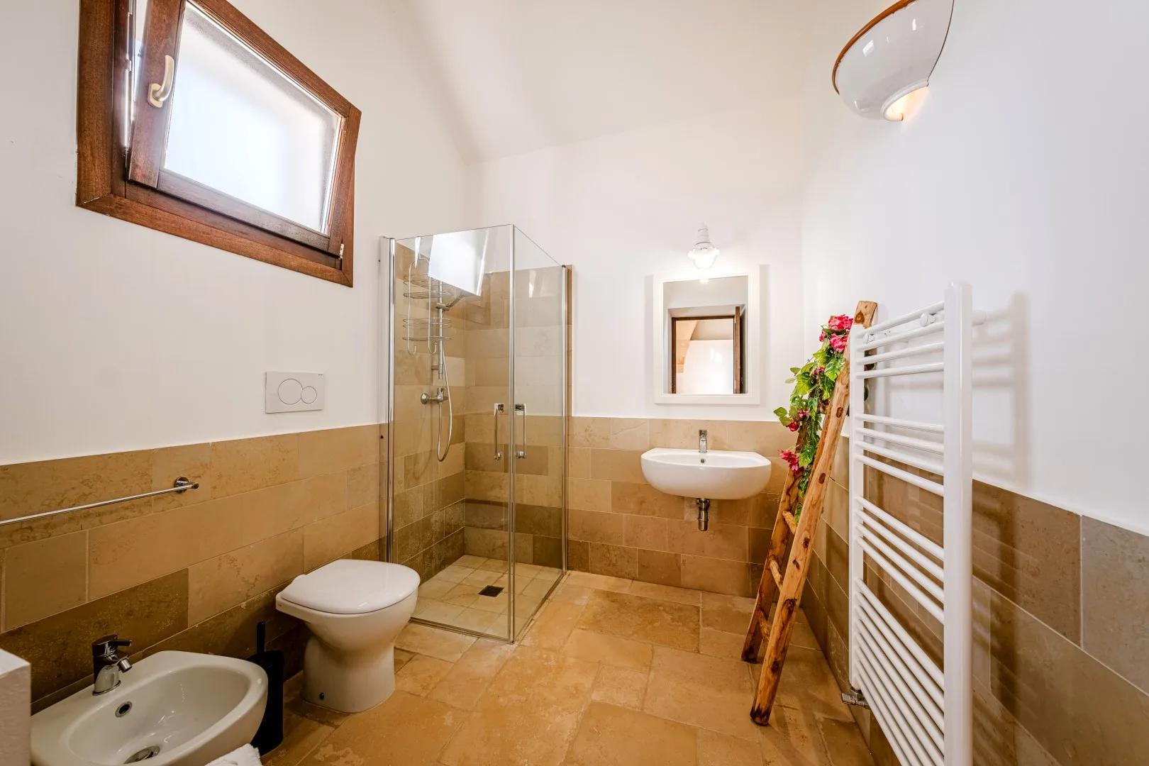 Un baño alicatado con ducha de cristal, lavabo suspendido, inodoro y toallero radiador.