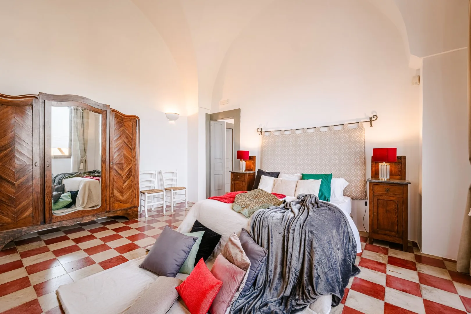 Un dormitorio con una cama grande, un armario de madera, mesitas de noche y suelo de baldosas ajedrezadas rojas y blancas.