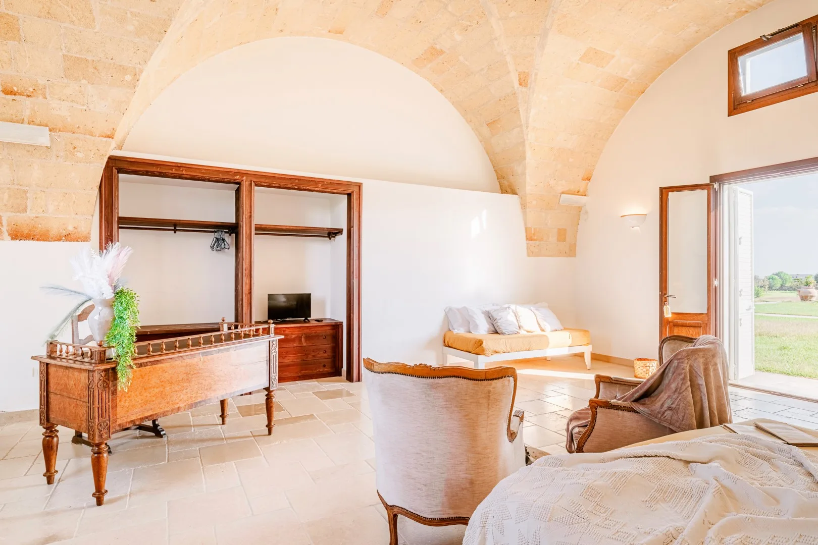 Un dormitorio luminoso con techo abovedado de piedra, armario de madera y una puerta abierta al exterior.