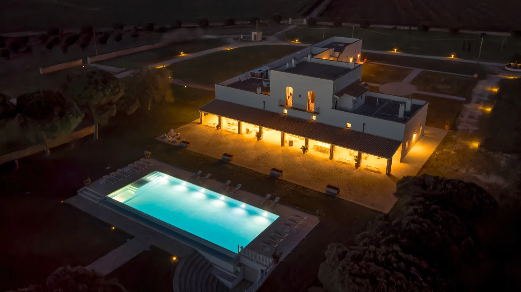 Un edificio moderno de techo plano brilla de noche junto a una piscina rectangular iluminada.