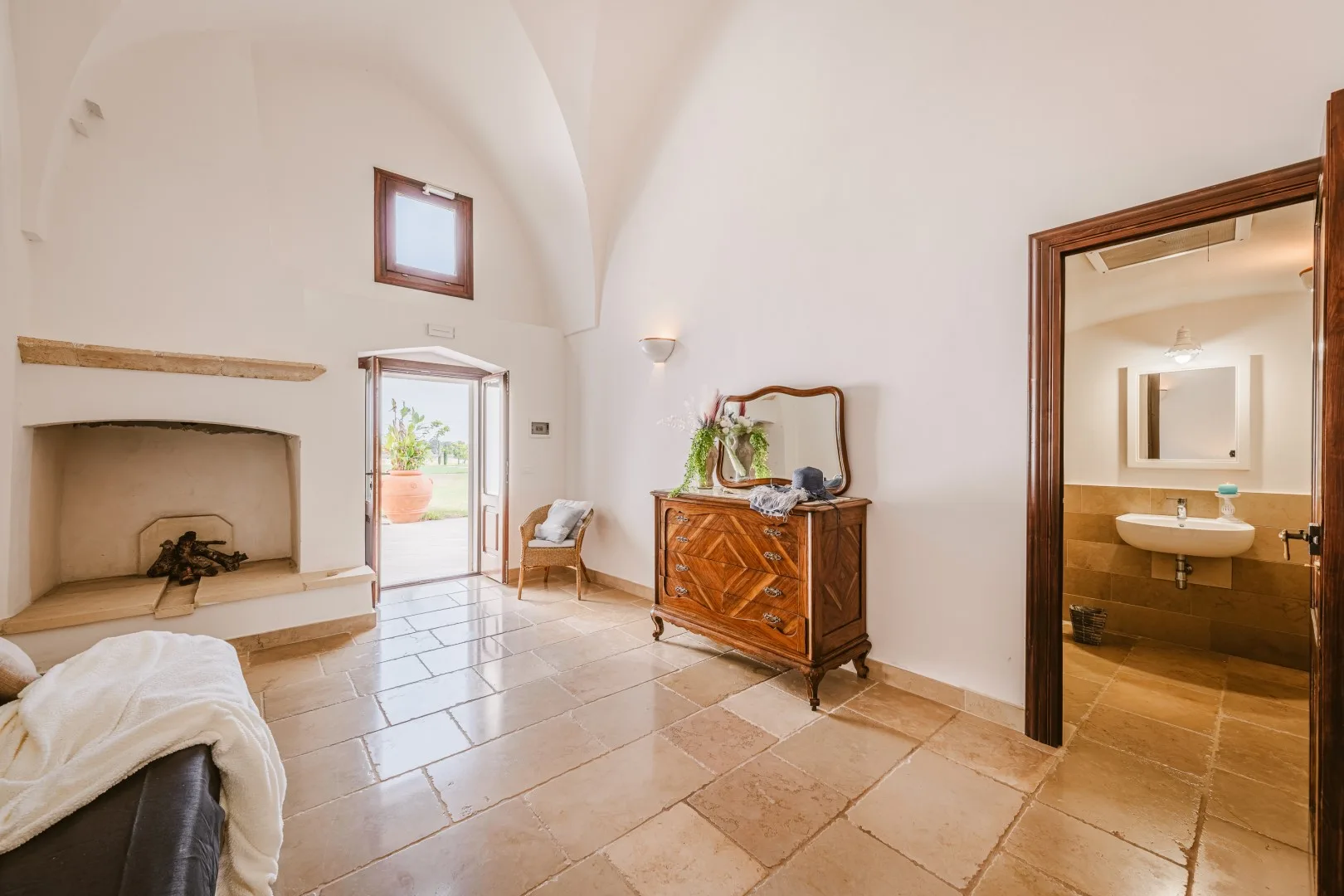 Una estancia luminosa con techos abovedados, una chimenea de piedra, un aparador antiguo y una puerta al baño.