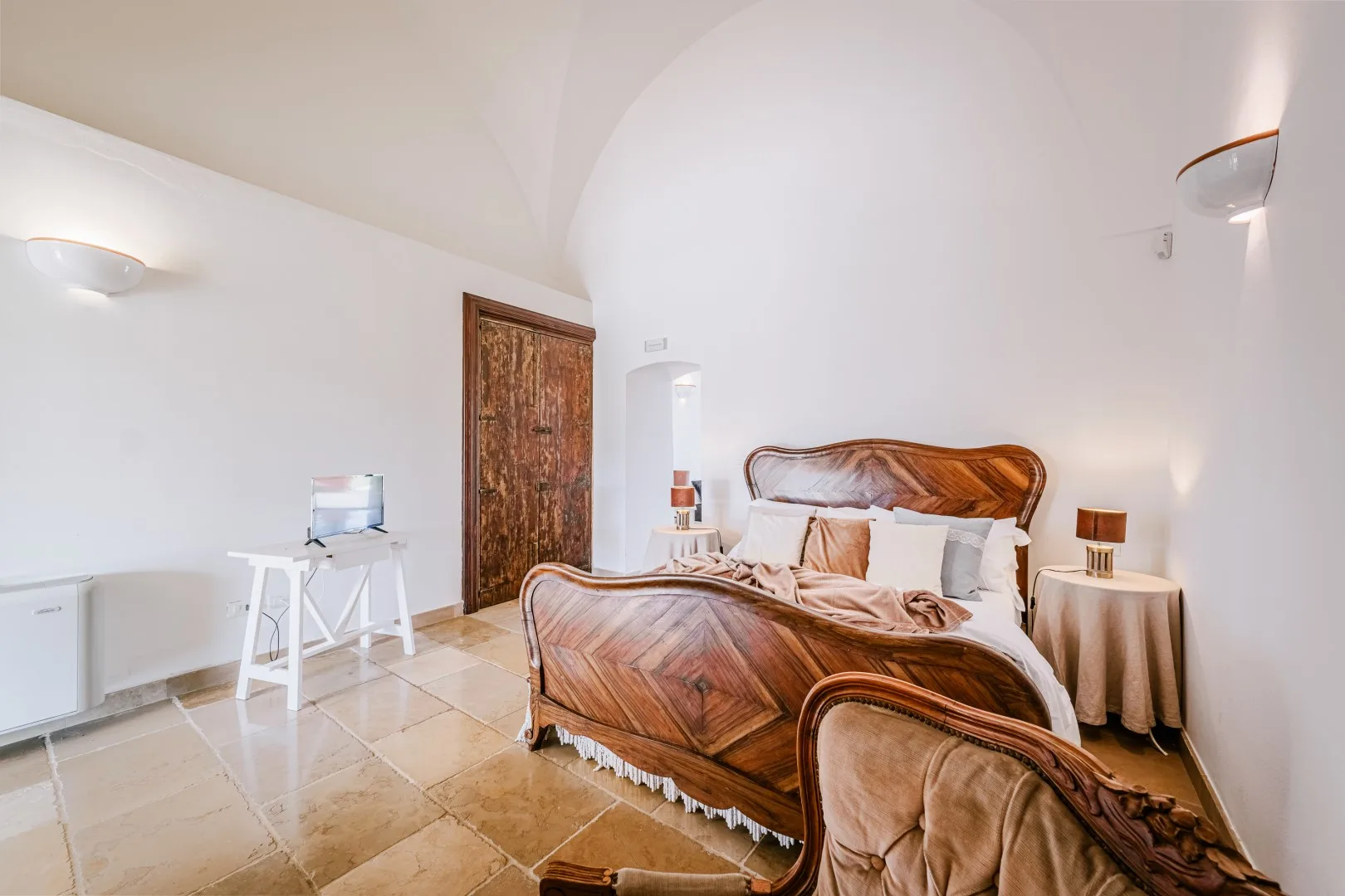 Un dormitorio con una cama de madera ornamentada, mesitas de noche y un pequeño televisor sobre una mesa.