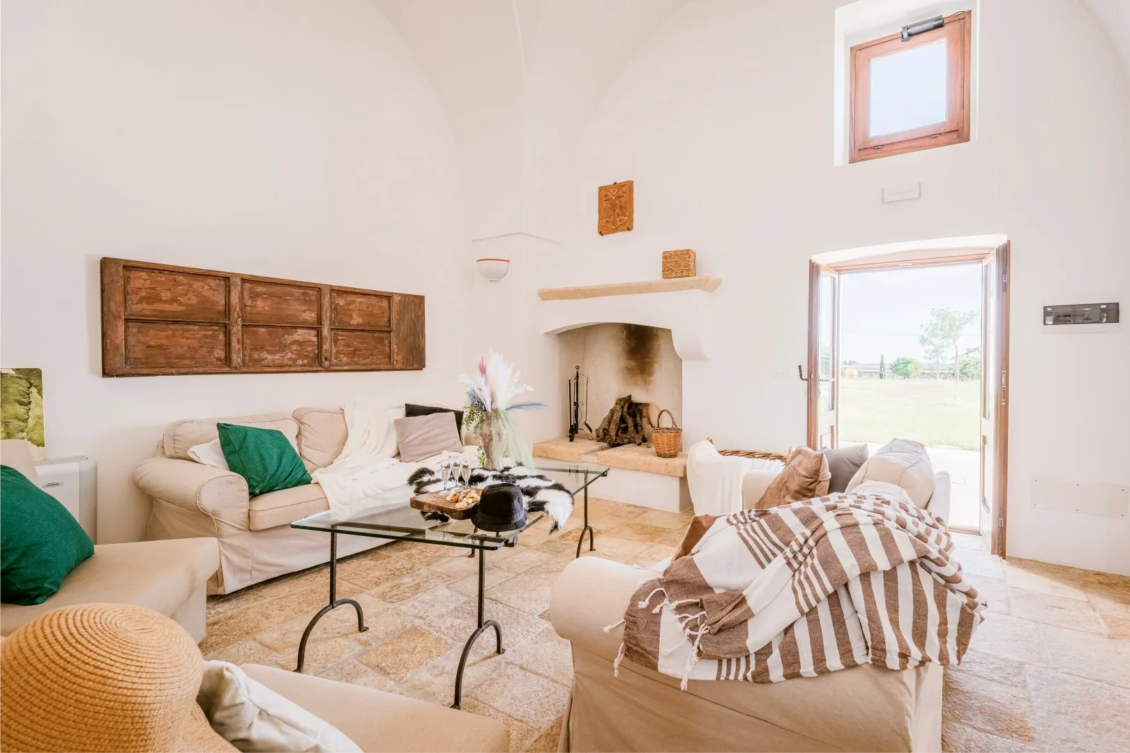 Una luminosa sala de estar con sofás color crema, una mesa de centro de vidrio y una chimenea rústica.