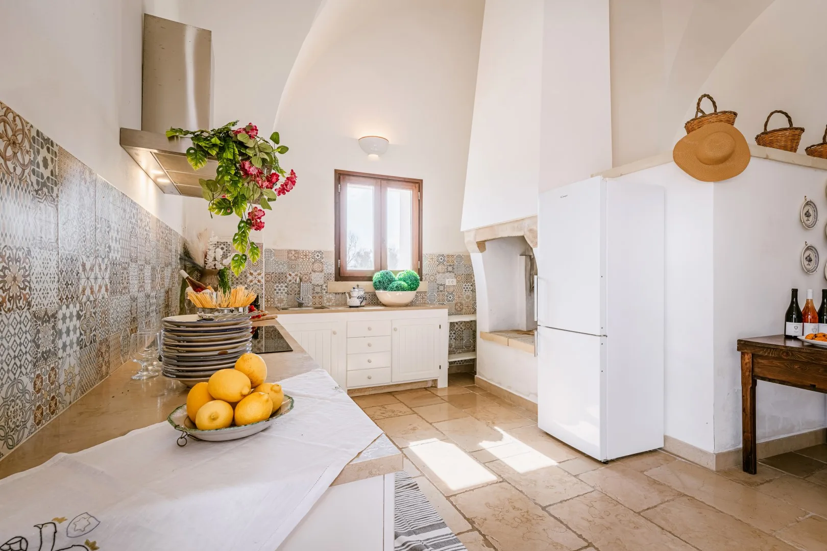 Una cocina luminosa con azulejos estampados, armarios blancos, un refrigerador grande y un frutero sobre la encimera.