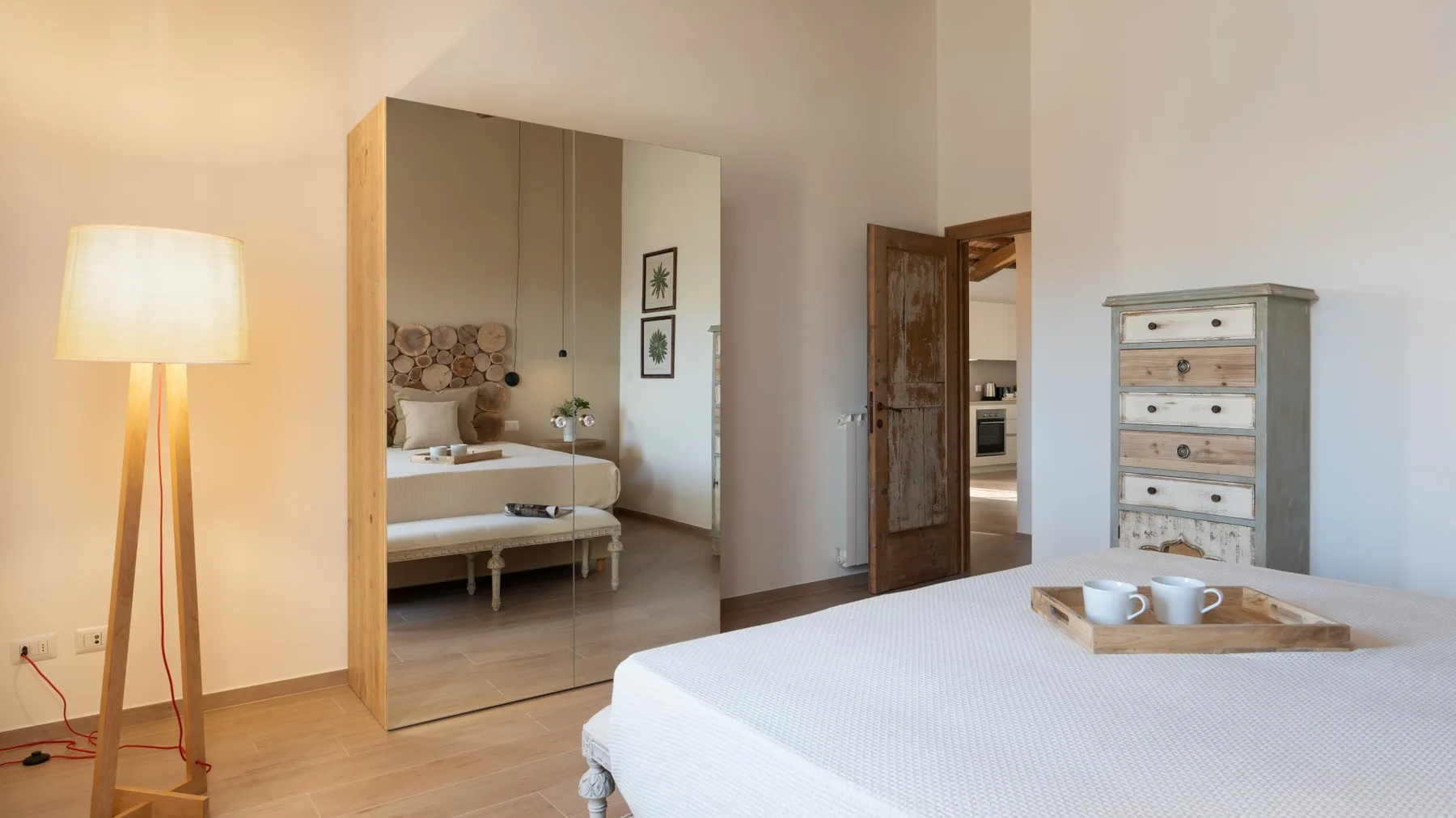 Un dormitorio luminoso con una cama grande, una lámpara de pie y una cómoda de madera.