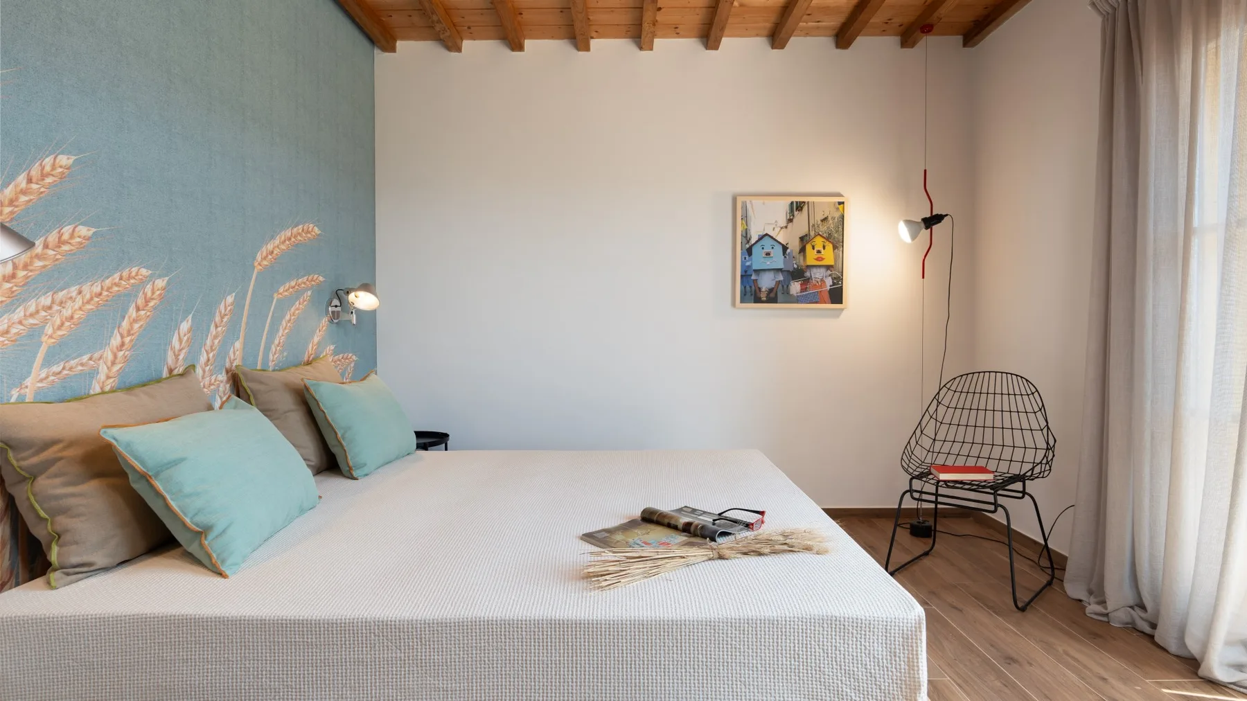 Un dormitorio con una cama, un mural decorativo y una silla de alambre.