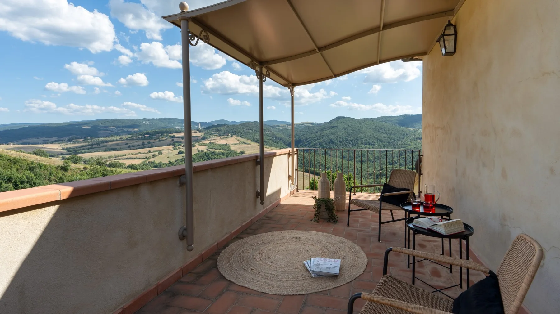 Una terraza cubierta tiene vistas a colinas, con asientos al aire libre y una mesita.