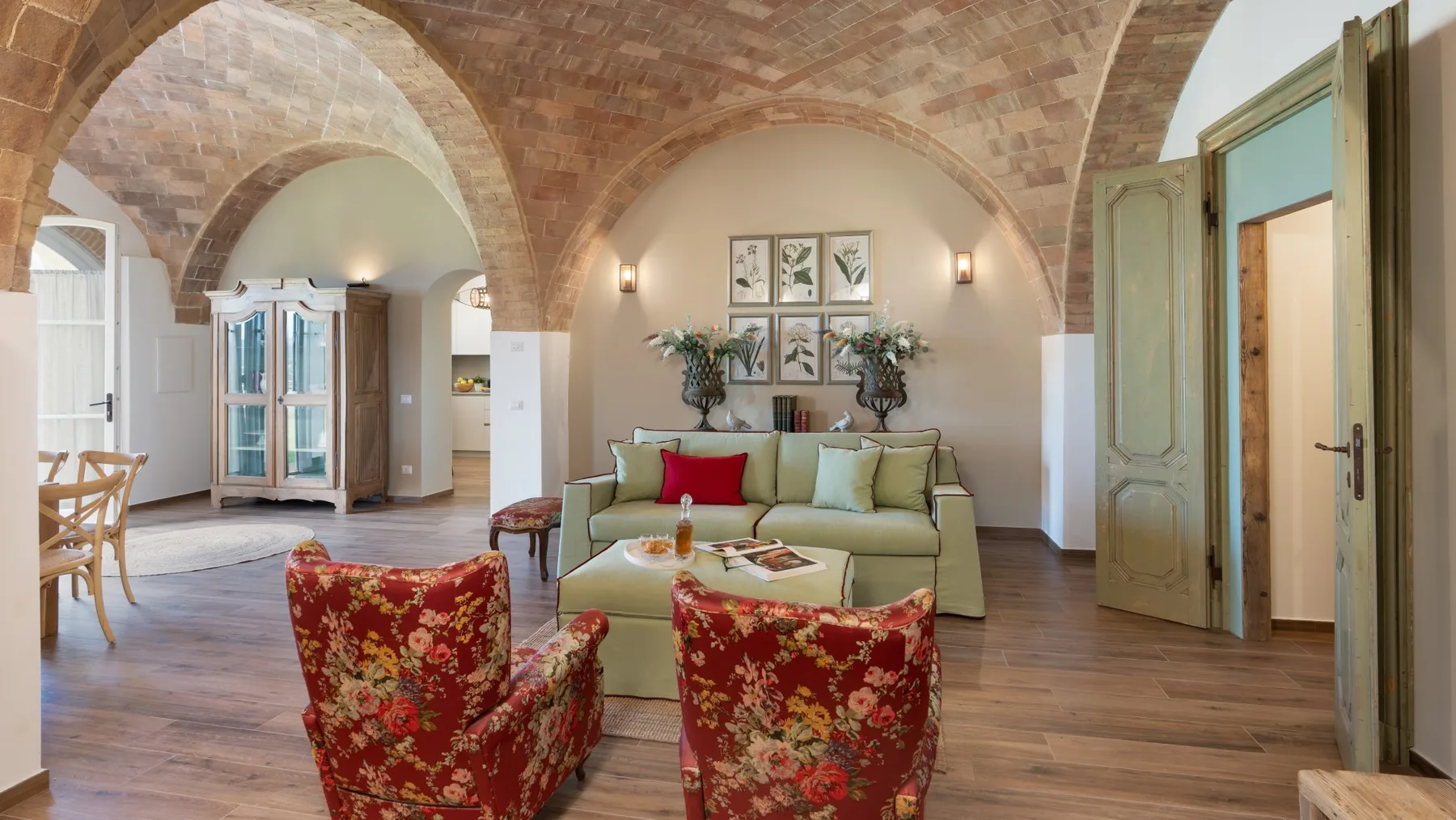 Una sala de estar con un sofá verde claro y dos sillones rojos florales.