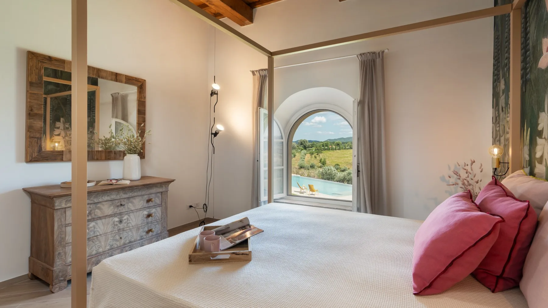 Un dormitorio con una cama grande y una ventana arqueada con vistas a colinas verdes.