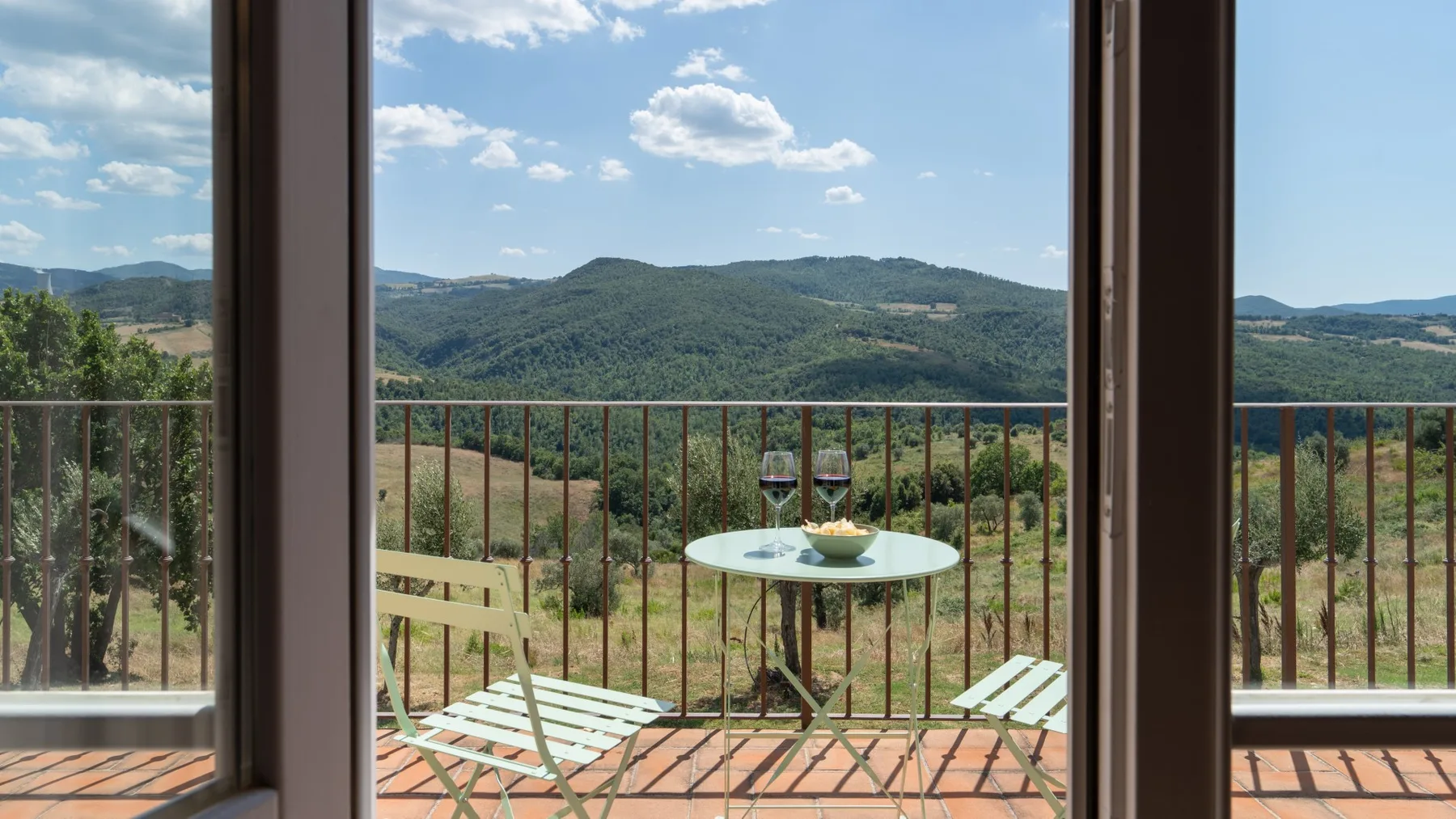 Un balcón con una mesa pequeña y asientos ofrece vistas a colinas verdes.