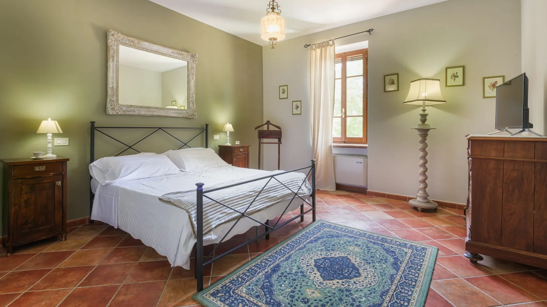 Un dormitorio con una cama de metal negro, ropa de cama blanca, una alfombra estampada y muebles de madera.