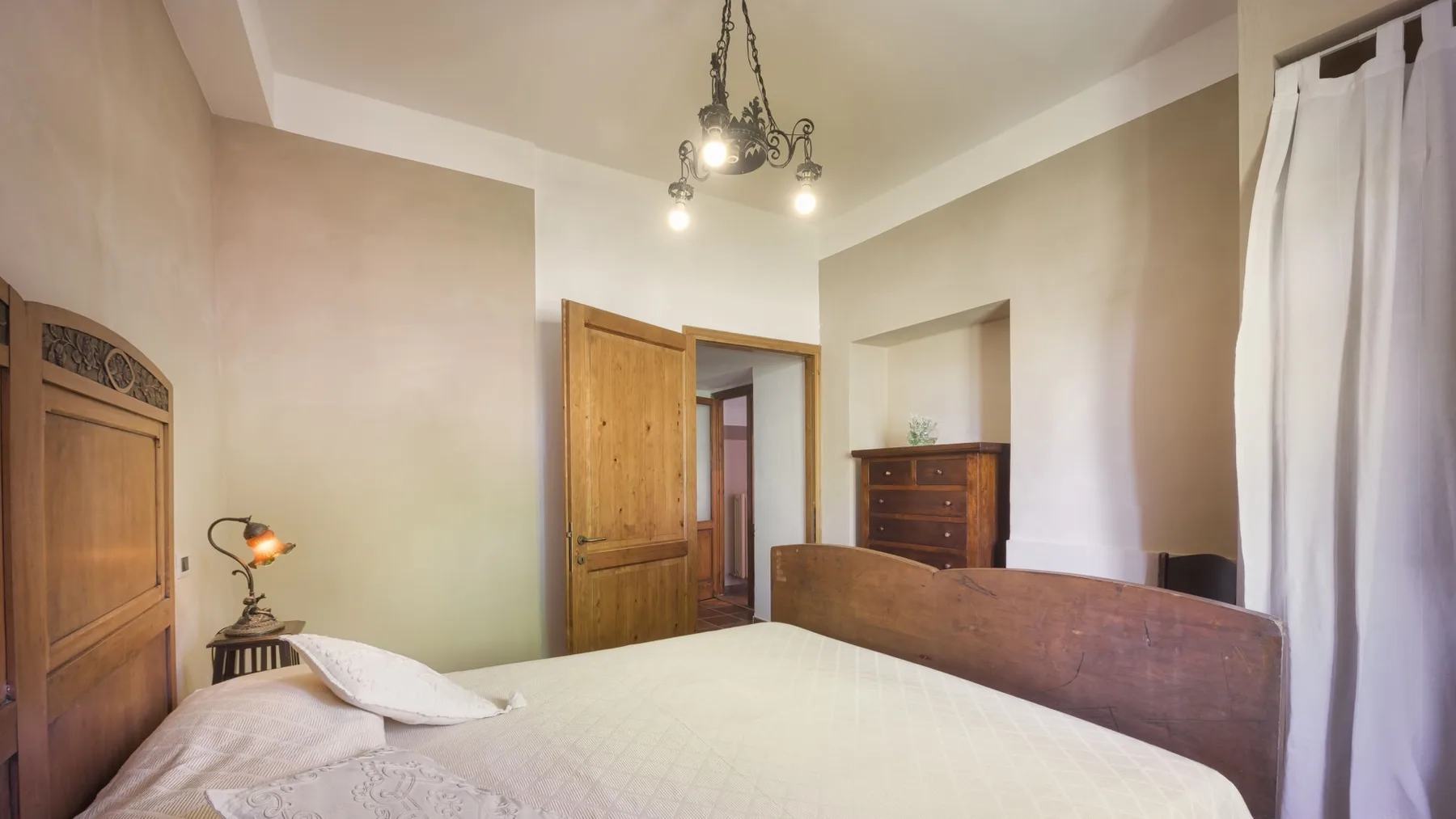 Un dormitorio con cama doble, cabecero de madera, puerta abierta y cómoda.