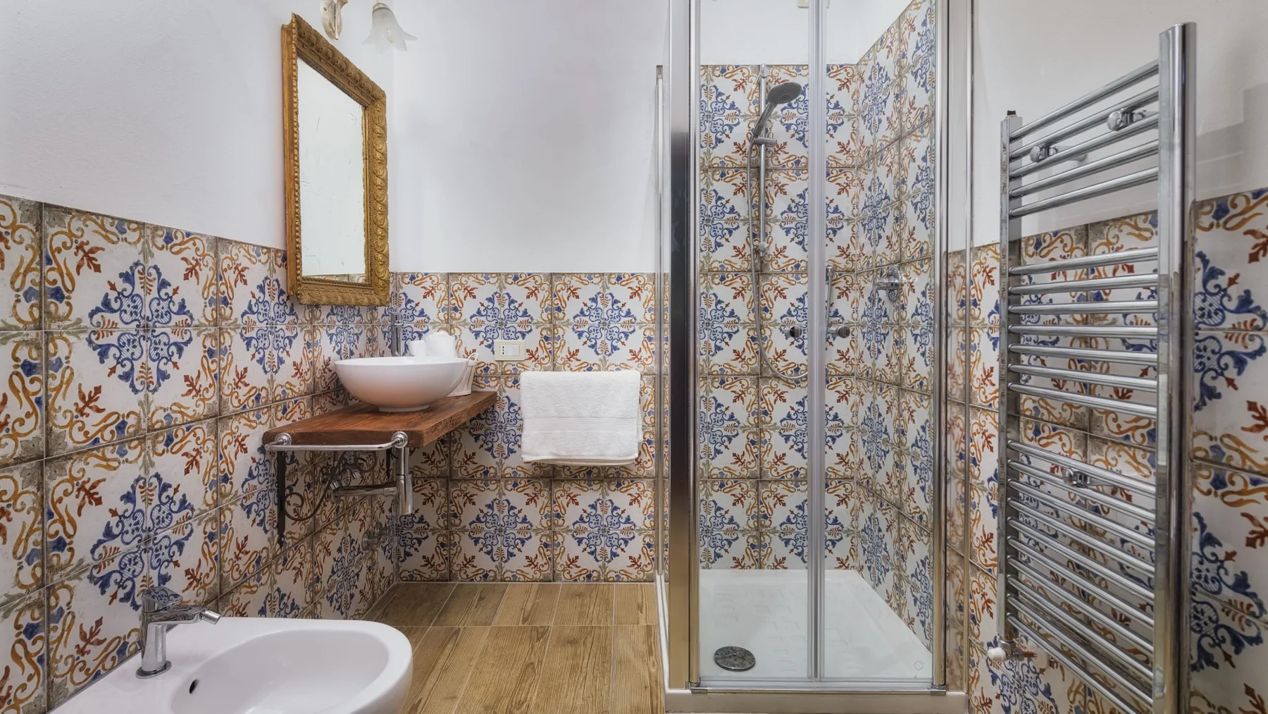 Baño alicatado con ducha de vidrio, lavabo suspendido y radiador toallero cromado.
