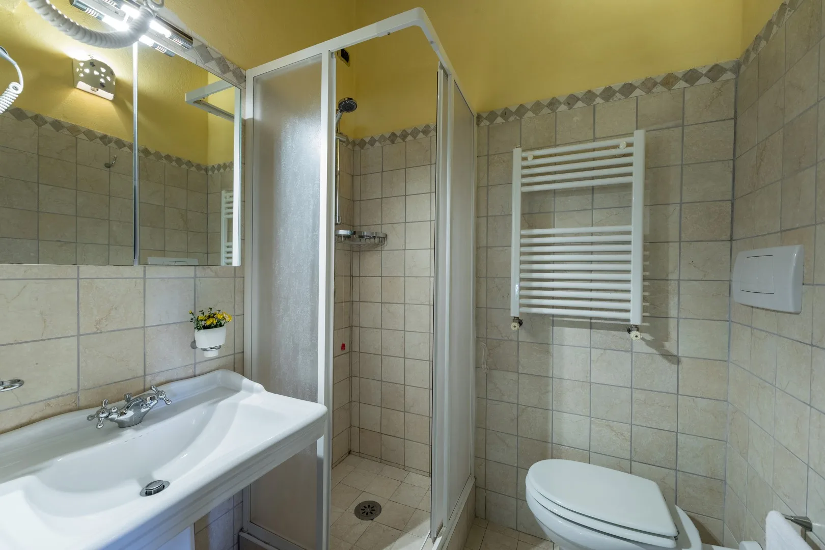Un baño alicatado con ducha de vidrio, lavabo y toallero calefactable.