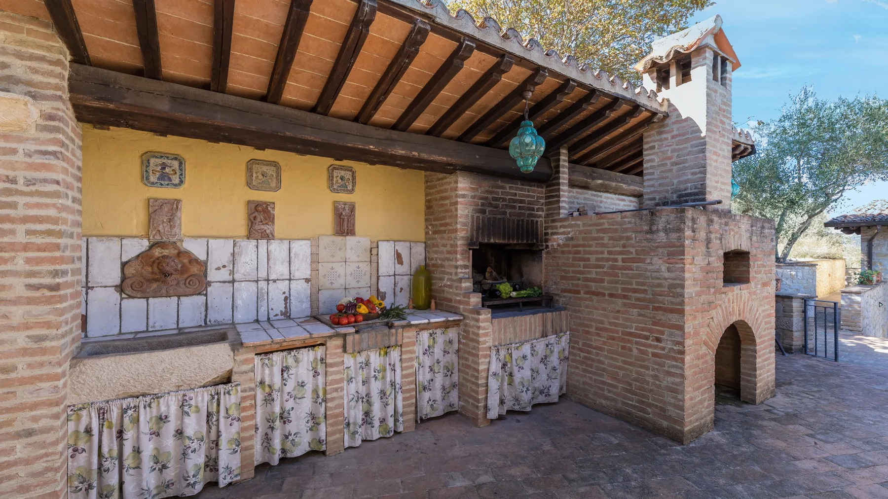 Una cocina exterior con un horno de ladrillo y una encimera de azulejos bajo un techo cubierto.