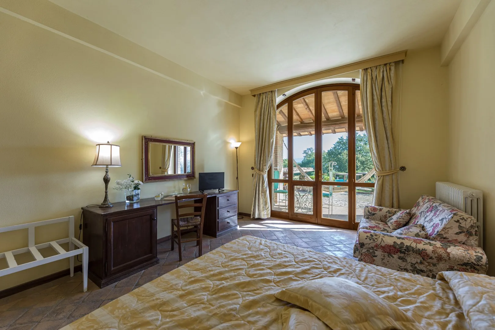 Un dormitorio con cama, escritorio y puertas de cristal que dan a un balcón.