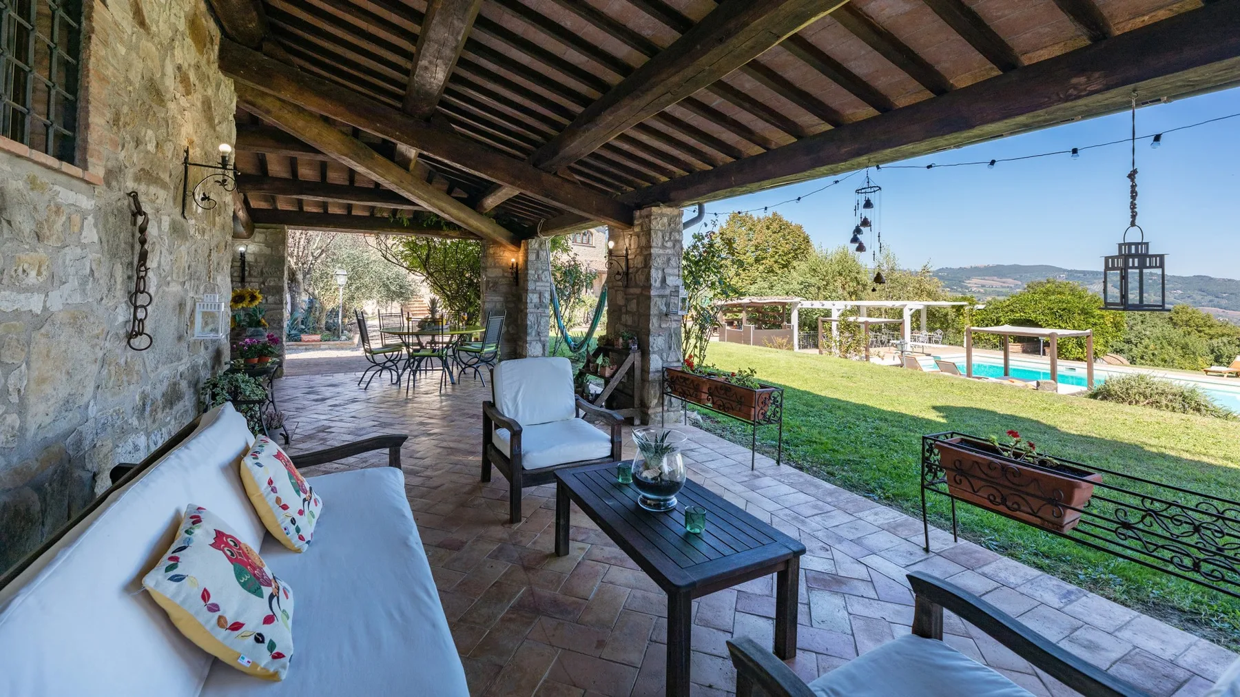 Un patio cubierto tiene asientos al aire libre con vistas al césped y a una piscina.