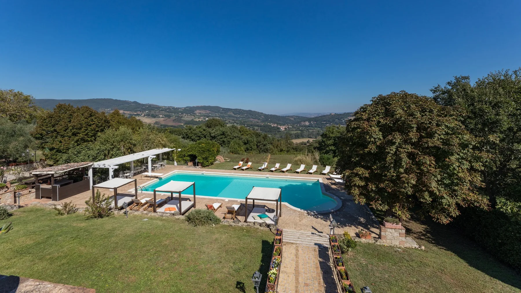 Una piscina al aire libre está rodeada de zonas verdes, con colinas a lo lejos.