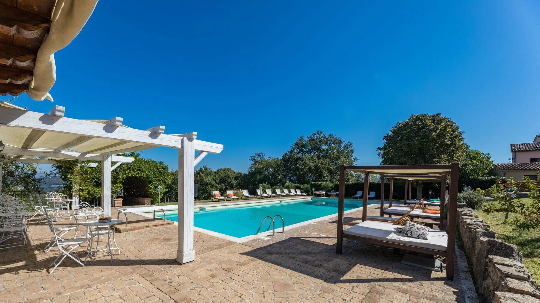 Una zona de piscina al aire libre con asientos de patio y una cama de día de madera a la sombra.