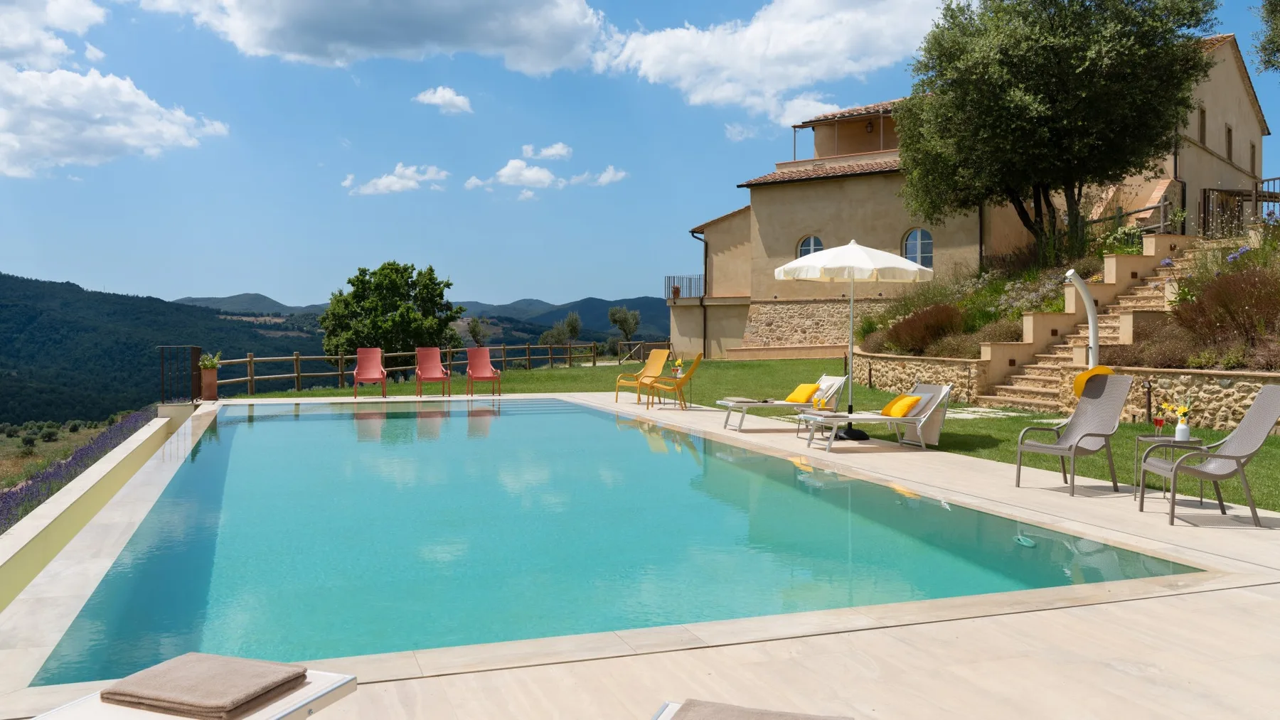 An outdoor swimming pool sits beside a hillside building with lounge seating.