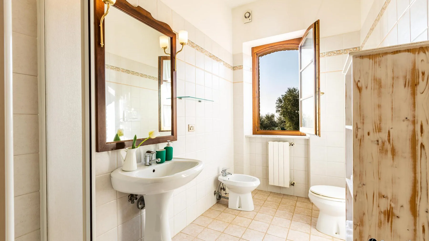 Un baño con azulejos, lavabo, inodoro y una ventana abierta.