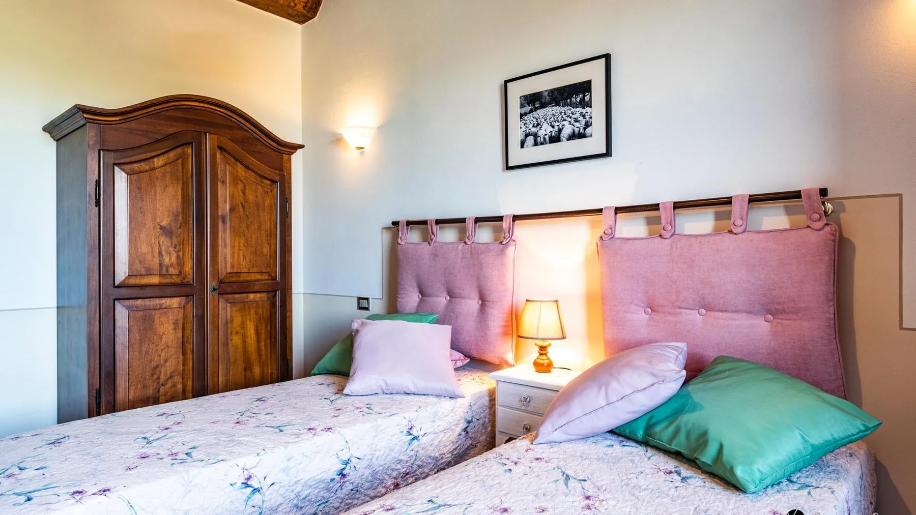 Un dormitorio con dos camas, cabeceros tapizados de color rosa y un armario de madera.