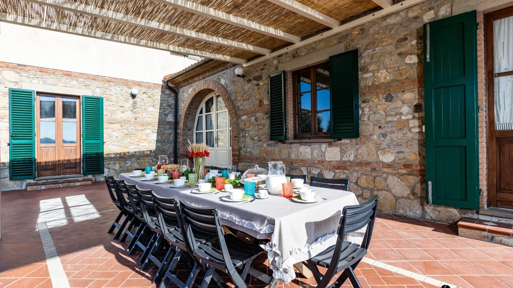 Comedor en un patio cubierto de piedra, con una mesa larga y asientos oscuros.