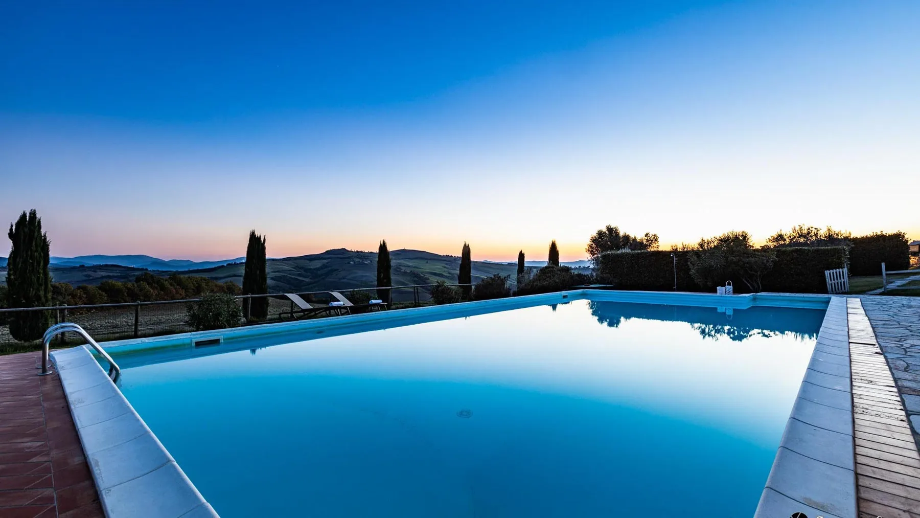 Una piscina al aire libre refleja el cielo del atardecer, con colinas visibles en el paisaje.