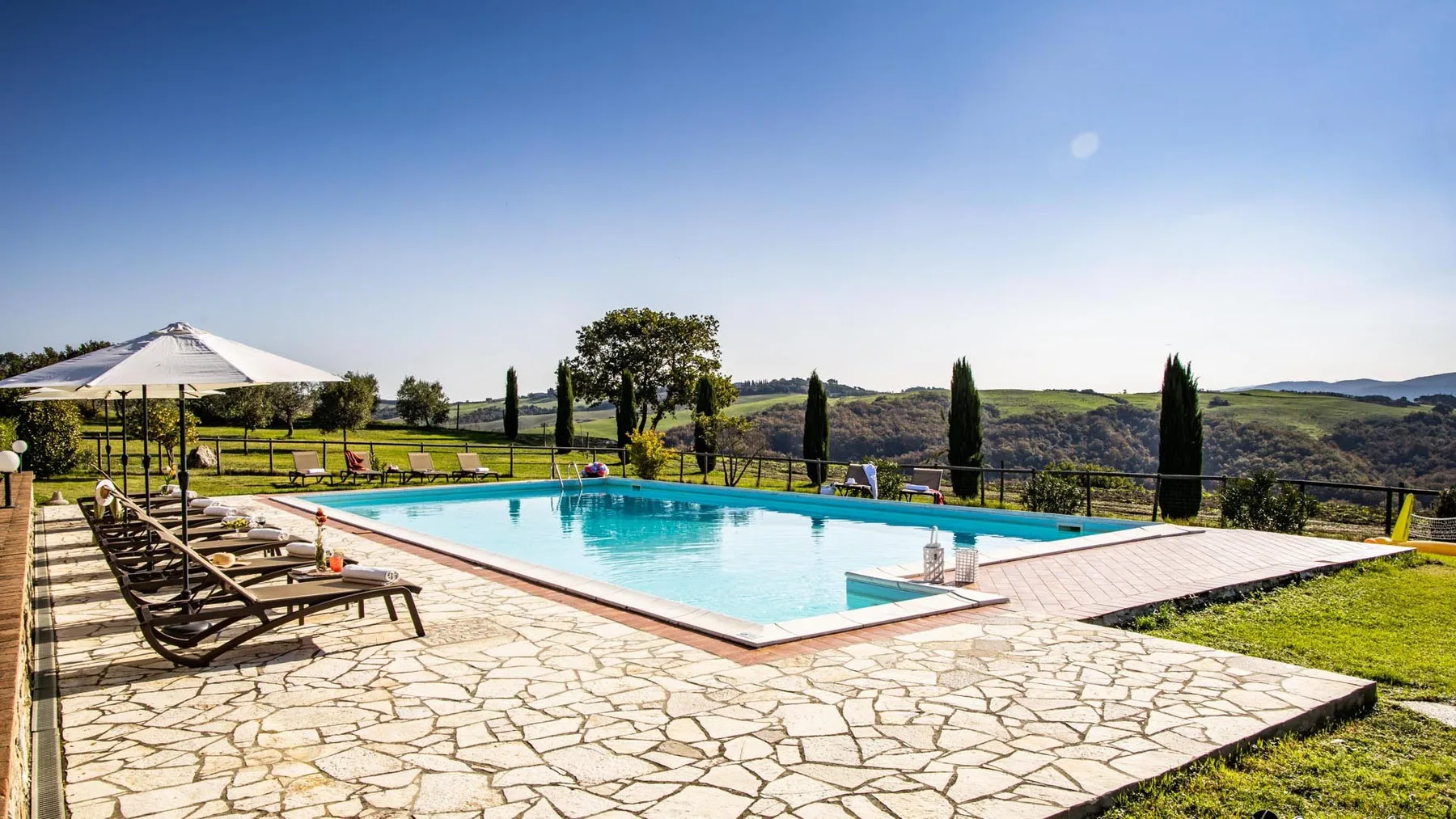 Una piscina al aire libre está junto a un patio de piedra con vistas a colinas verdes.