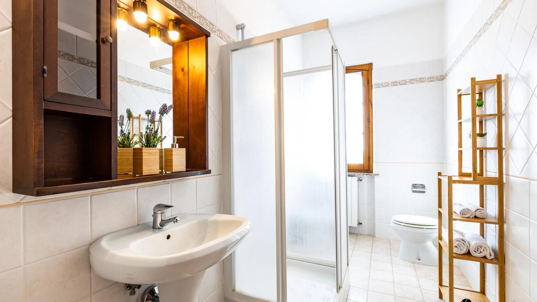Un baño luminoso con lavabo, ducha, inodoro y estantería de madera.