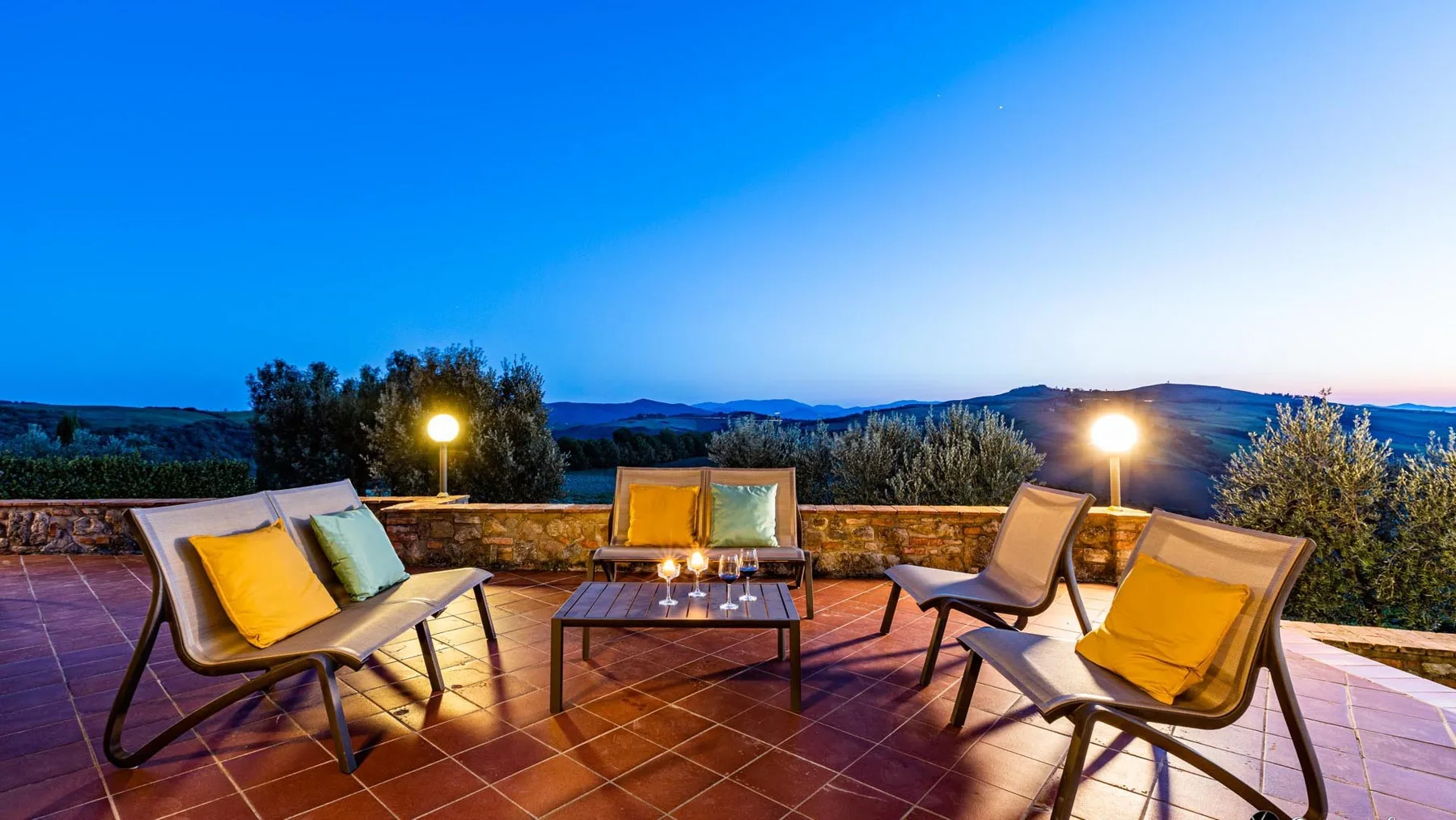 Una terraza exterior tiene asientos y una mesa baja con vistas a las colinas.